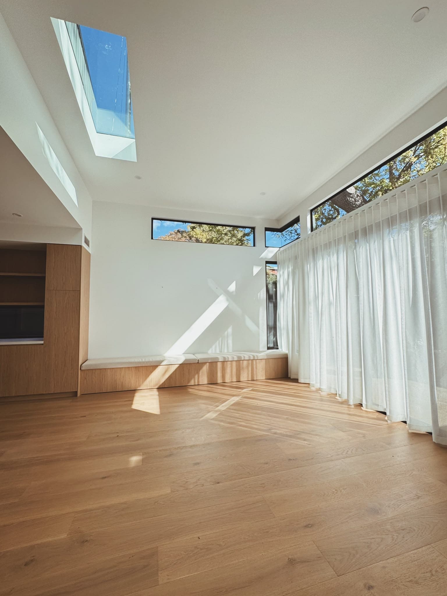 Sunlit open-plan living space with skylight and sheer curtains, residential new build