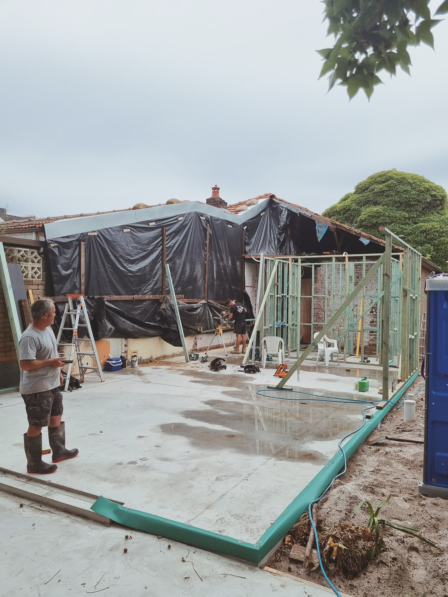 Residential alteration mid-construction, roof framing and site preparation underway