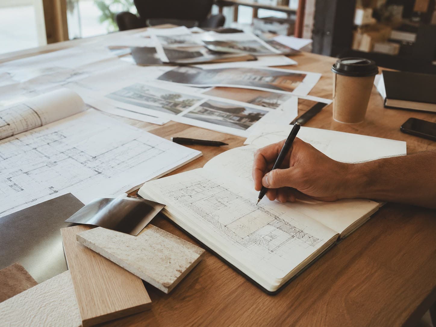 Hand-drawn floor plan sketch alongside printed architectural photos and material samples on a desk
